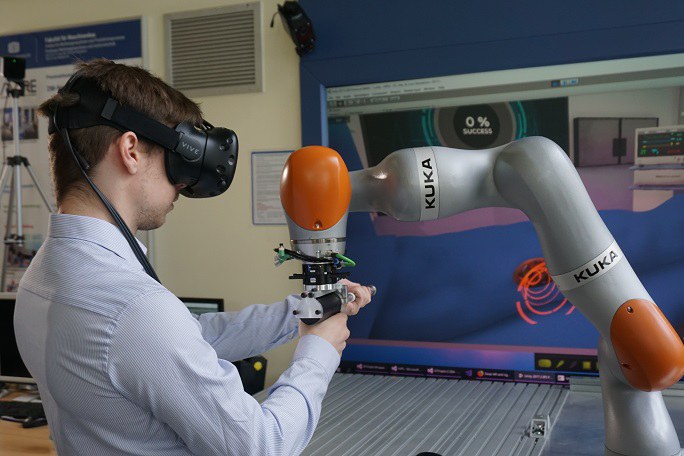 Mann mit VR-Brille arbeitet an einem Gerät, das von einem Roboterarm gehalten wird