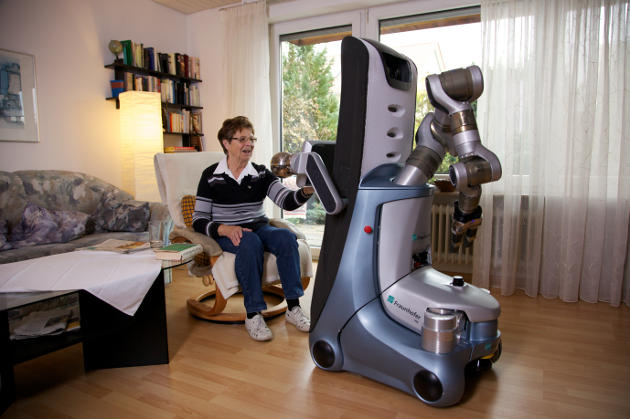 Eine Frau in einem Sessel nimmt etwas von einem Roboter entgegen.