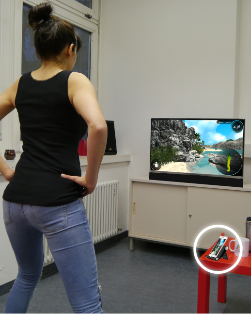 Eine Frau trainiert vor einem Bildschirm. Auf dem Bildschirm sieht man wie in einem Computerspiel große Felsen, Sand und Meer.  