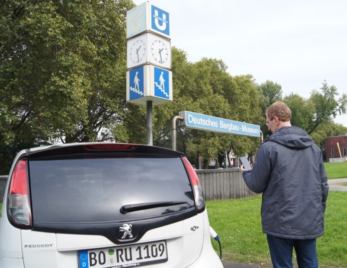 Mann steht neben einem Auto und schaut auf sein Handy.