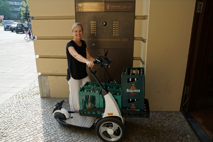 Eine Frau mit einer Art Fahrrad ohne Sitz, im Hintergrund sind Bierkästen.