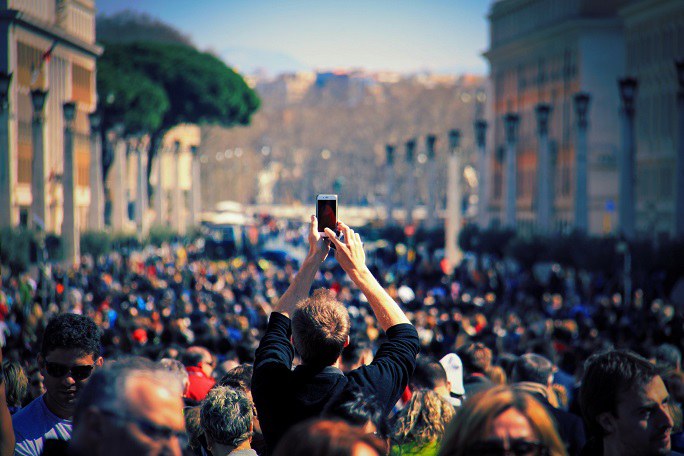 Ein Mann in einer Menschenmenge hält sein Smartphone in die Höhe, um ein Foto zu machen.