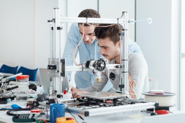 Zwei Männer hinter einem 3D-Drucker.