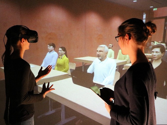 Eine Frau mit VR-Brille, die vor einer virtuellen Zuhörerschaft spricht.