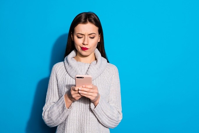 Eine junge Frau schaut skeptisch und misstrauisch auf ihr Smartphone