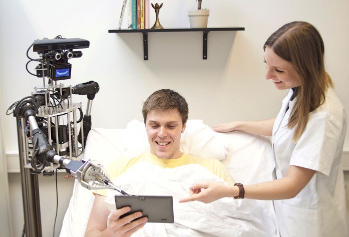 Ein Roboter und eine Krankenschwester, die zusammmen mit einem Patienten auf ein Tablet schauen. 