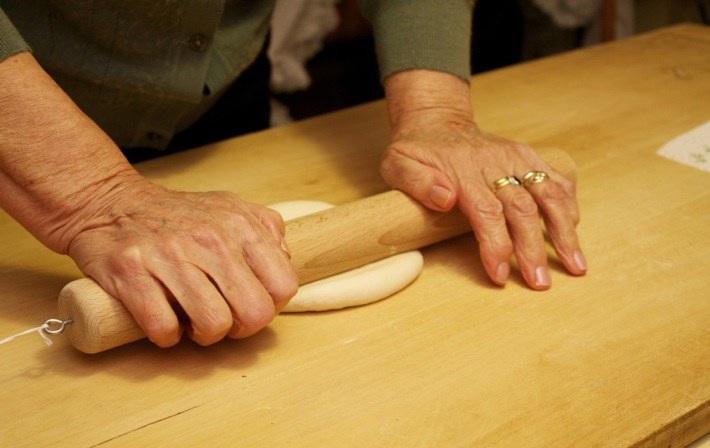 Jemand der einen Teig mit einer Holzstange rollt. 