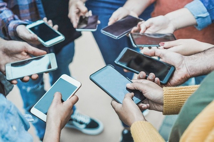 Junge Menschen stehen im Kreis und halten ihre Smartphones in die Mitte.