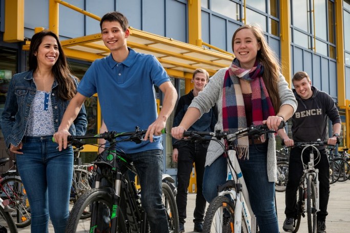 Mehrere Jugendliche stehen mit ihren Fahrrädern vor einem Gebäude
